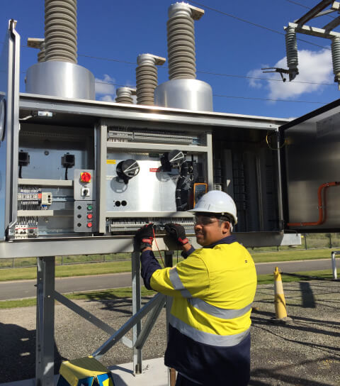 Electrical technician in high-visibility gear and helmet performing high voltage maintenance on an electrical panel with insulators Electrical technician in high-visibility gear and helmet performing high voltage maintenance on an electrical panel with insulators